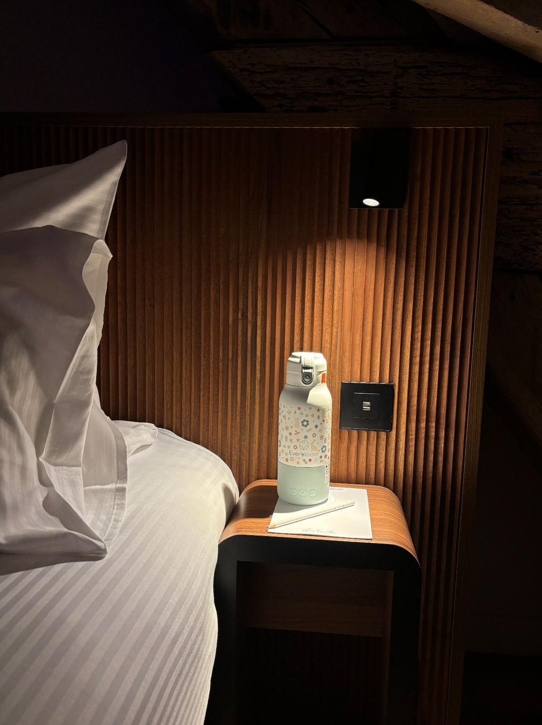 Chauffe-biberon nomade Warm & Go Everbloom posé dans une chambre d’hôtel à l’éclairage chaleureux